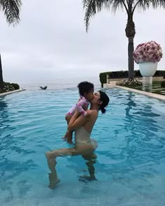 a woman is holding a child in the water near a swimming pool with palm trees