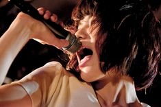 a woman singing into a microphone while holding her hand up to the side of her head