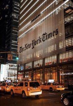 the new york times building is lit up at night with taxi cabs parked in front