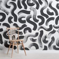 a wooden chair sitting in front of a wall with black and white designs on it