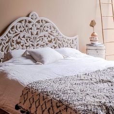 the bed is made with white linens and has a decorative headboard on it