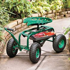 a small green cart with wheels sitting on the ground in front of some plants and bushes