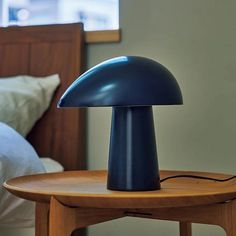 a blue lamp sitting on top of a wooden table next to a night stand with a bed in the background