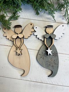 two wooden angel ornaments sitting on top of a white wood floor next to evergreen branches