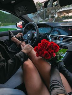 a woman sitting in the driver's seat of a car holding a bouquet of red roses