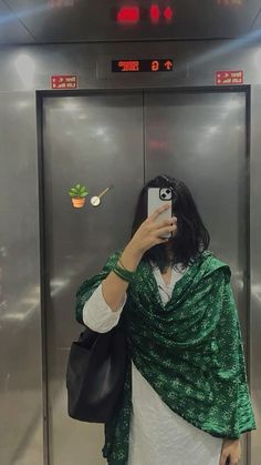 a woman taking a selfie with her cell phone in front of an elevator door