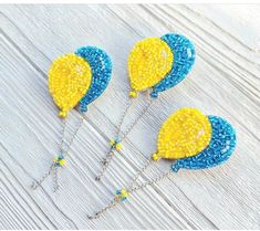 three blue and yellow beads are attached to silver chains on a wooden table with white boards