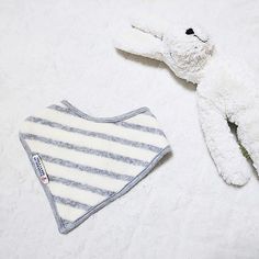 a white stuffed animal laying next to a baby bib on a bed with a striped blanket