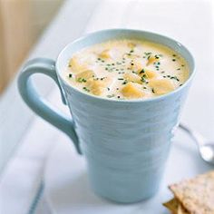 a white plate topped with a blue cup filled with soup and crackers next to it