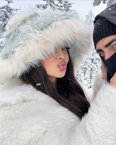 a man and woman standing in the snow wearing winter clothes, covering their faces with gloves