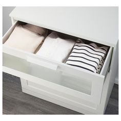 an open drawer on the side of a white dresser with folded towels and pillows in it