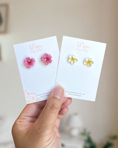 two small pink and yellow flowers are held up in front of each other by a person's hand