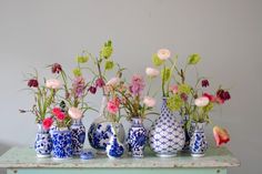 a group of vases with flowers in them on a table next to a wall