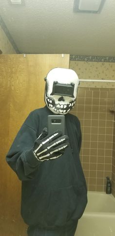 a person wearing a skeleton mask and holding a cell phone in a bathroom with tiled walls