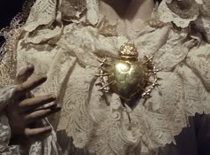 a close up of a woman's white dress with a gold heart brooch