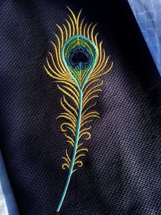 a close up of a peacock feather on a black piece of cloth with gold thread