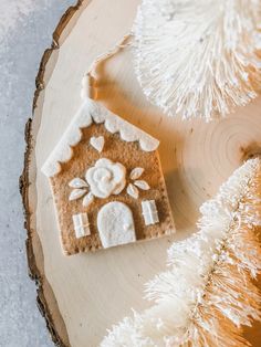 a gingerbread house is decorated with white icing on a piece of wood next to a christmas tree