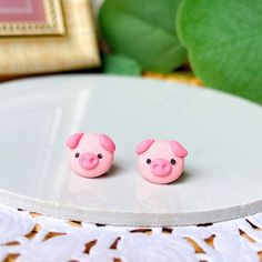 two pink pig earrings sitting on top of a white plate next to a green plant