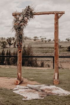 a wooden arch decorated with flowers and greenery on top of a grass covered field