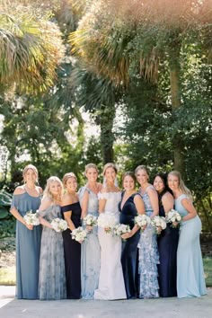 a group of women standing next to each other in front of some trees and bushes