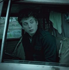 a young man sitting in the back seat of a car looking at something off to the side