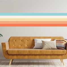 a couch with pillows on it in front of a wall painted with multicolored stripes