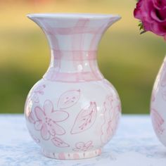 two white vases with pink flowers in them sitting on a blue table cloth next to each other