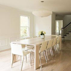 a dining room table with white chairs in front of it and stairs leading up to the second floor