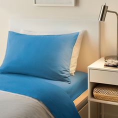 a bed with blue sheets and pillows in a bedroom next to a lamp on a nightstand