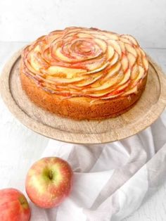 an apple cake on a wooden plate next to two apples