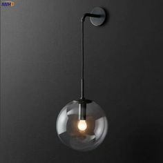 a glass ball light hanging from the side of a wall with a metal hook on it