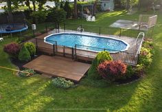 an above ground pool surrounded by lush green grass and trees, next to a deck