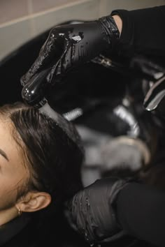 a woman is getting her hair cut by someone in black gloves and rubber gloves on