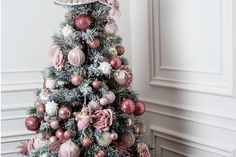 a decorated christmas tree with pink and silver ornaments on it's branches in a white room