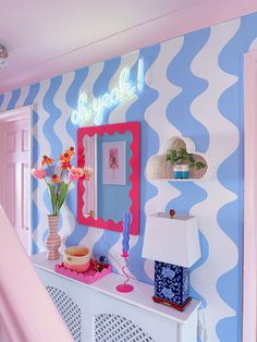 a room with blue and white stripes on the walls, pink accents and flowers in vases