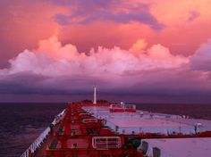 the back end of a ship with clouds in the sky and water behind it at sunset