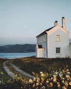 a white house sitting on top of a lush green field next to the ocean and mountains