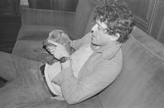 a black and white photo of a man sitting on a couch holding a small dog