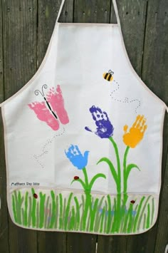 an apron with painted flowers on it hanging from the side of a wooden fence,