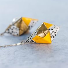 two yellow and white origami earrings hanging from a chain on a gray surface