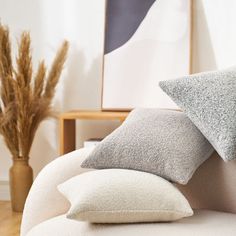 two gray and white pillows sitting on top of a bed next to a vase with dry grass