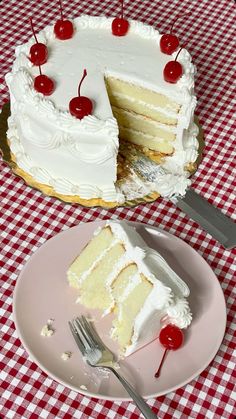 a piece of cake with white frosting and cherries on top is sitting next to a slice of cake that has been cut