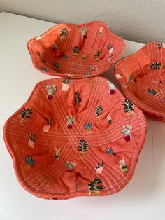 two orange bowls sitting on top of a white table next to each other, with designs on them