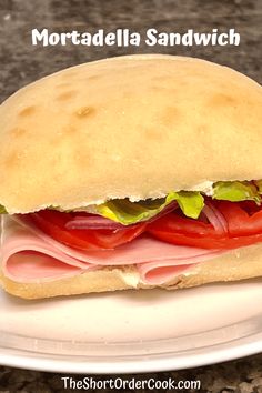 a sandwich with ham, lettuce and tomato on it sitting on a plate