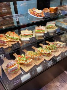 a display case filled with lots of sandwiches and other foods on wooden cutting boards next to each other