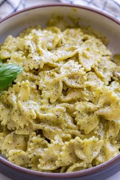 a bowl filled with pasta and pesto on top of a white table cloth next to a green leaf