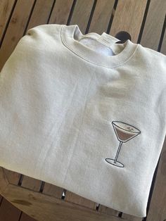 a t - shirt with a martini glass embroidered on the front and side, sitting on a wooden table