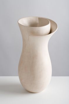 a white vase sitting on top of a table next to a gray wall and floor