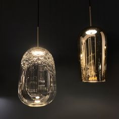 two glass lamps hanging from the ceiling in a dark room, one is clear and the other is gold