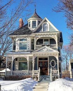 a white victorian house with snow on the ground and trees around it, in winter